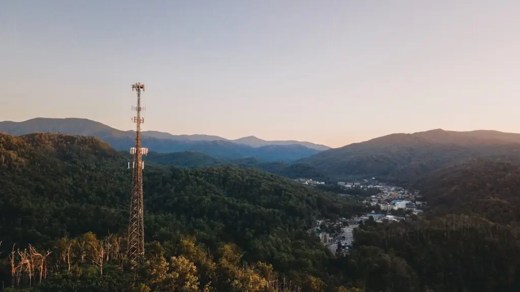 Broadcast tower on a forested ridge above a small tourism town at sunrise, the regional reach behind a bundled radio and digital campaign.