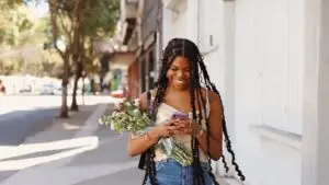 near-me-searches-customer-phone-ozarks - Marketing Agency in Branson MO | Smart & Simple Communications - Marketing Agency in Branson MO | Smart & Simple Communications Customer walking a sunny small town sidewalk, smiling at her phone with fresh flowers from a local shop she found through a near me search