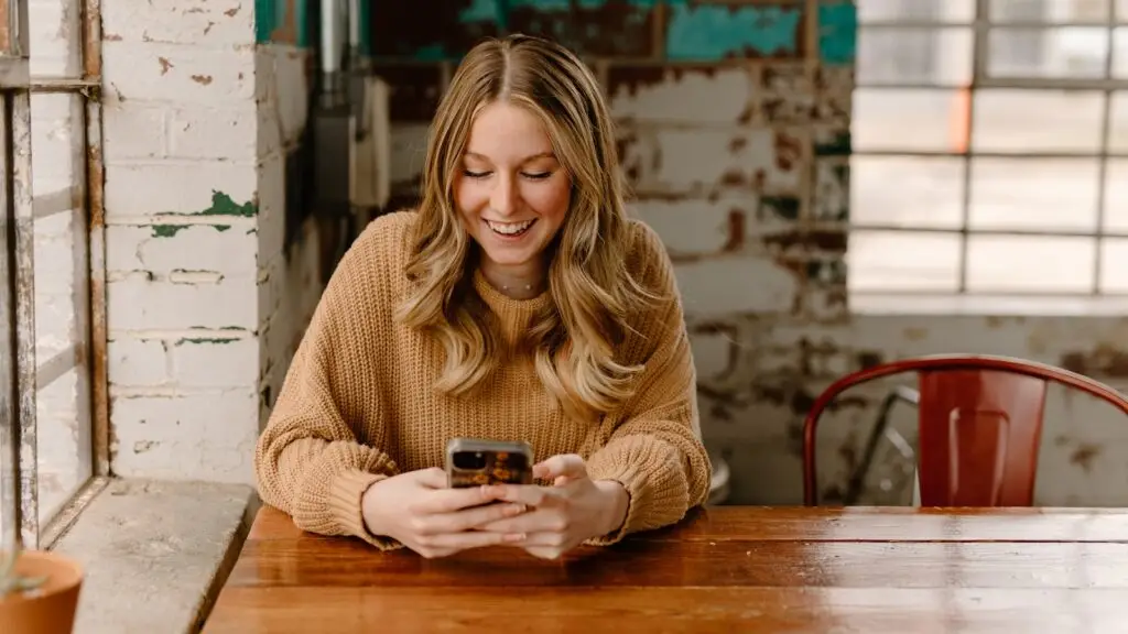 Woman browsing a local business website on her smartphone at a cafe table, showing the mobile experience most customers get first.