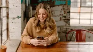 Woman browsing a local business website on her smartphone at a cafe table, showing the mobile experience most customers get first.