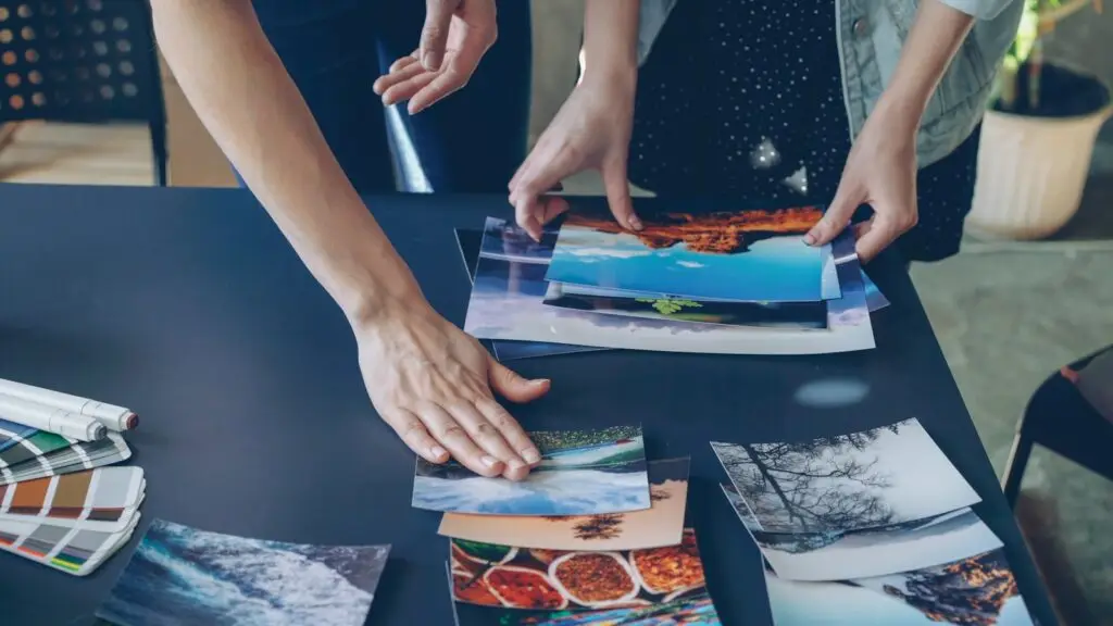 Marketing agency creative team arranging photo prints and color swatches on a table while planning an ad campaign for a small business