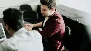 In-house marketing vs agency decision - Smart & Simple Communications - Smart & Simple Communications Two people shaking hands across a desk beside a laptop, the moment a Branson business owner decides between hiring in house marketing and bringing in an outside team.
